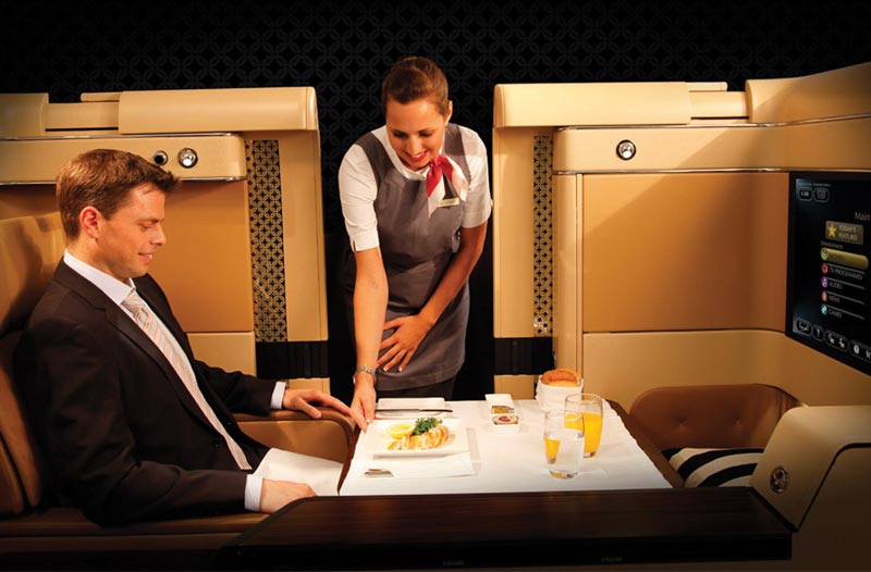 Ein First Class Reisender wird in der Diamond First Class Suite von Etihad Airways von einer Stewardess bedient.