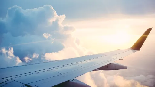 Blick auf den Fl&uuml;gel eines Flugzeugs &uuml;ber den Wolken mit der Sonne am Horizont
